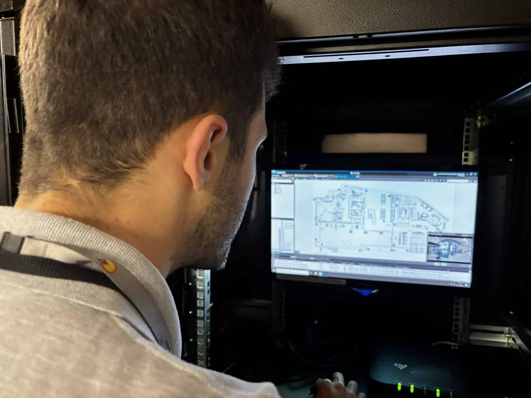 Man looking at a computer monitor displaying a building floor plan in a server room.