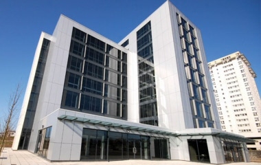 Modern glass office building with multiple stories against a clear blue sky.