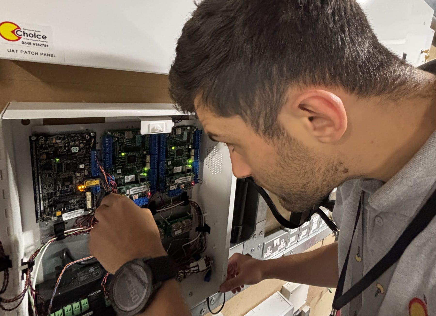 A man works on wiring inside an open electrical control panel.