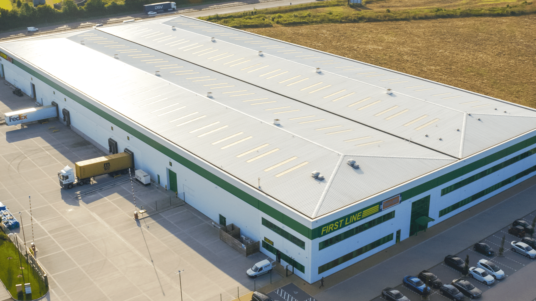 A large automotive parts distribution center with trucks and cars parked outside.