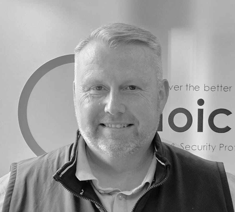 LeeEvans A man smiling in front of a sign, shown in black and white.