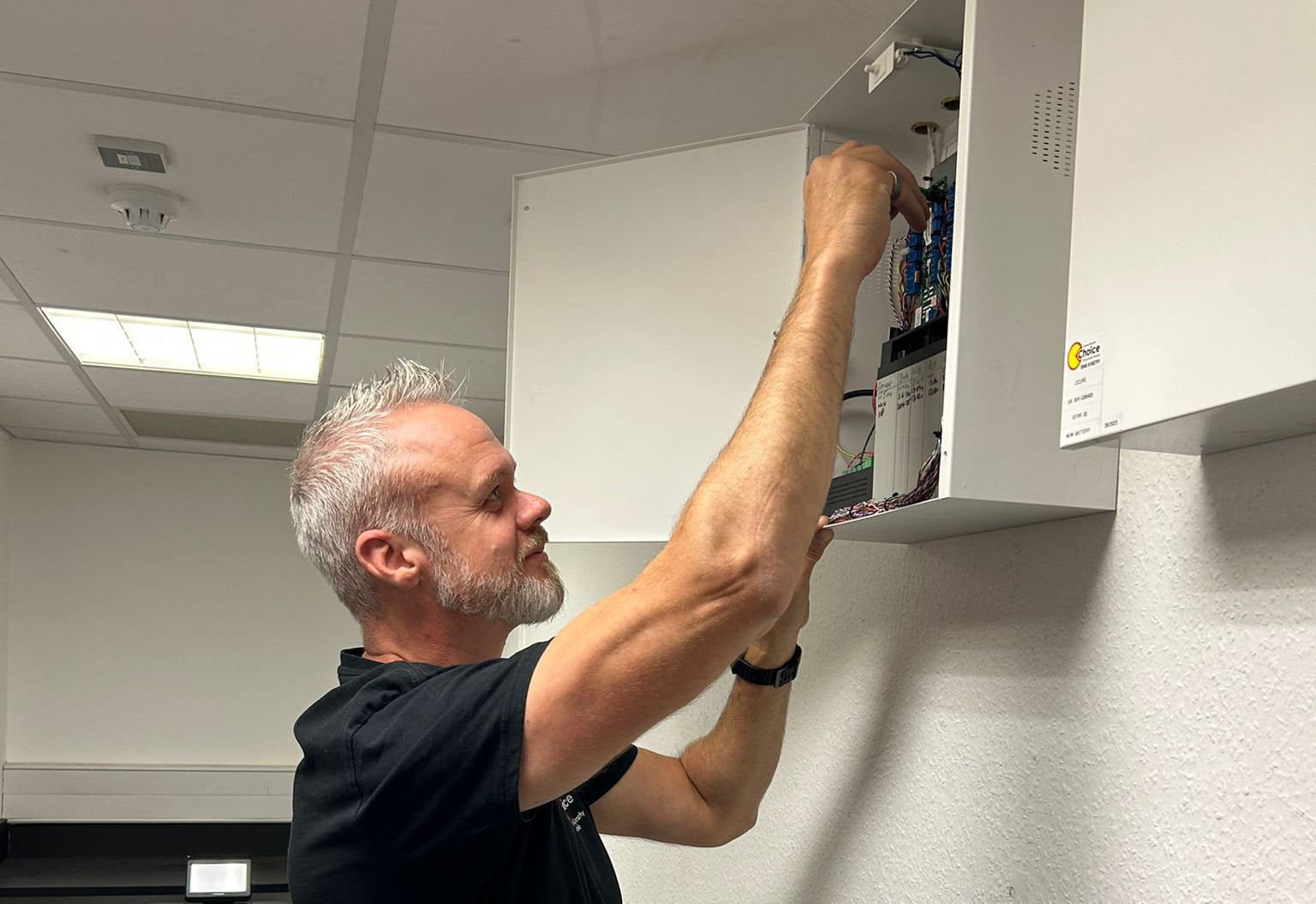 Man performing maintenance on electrical panel mounted on a wall.