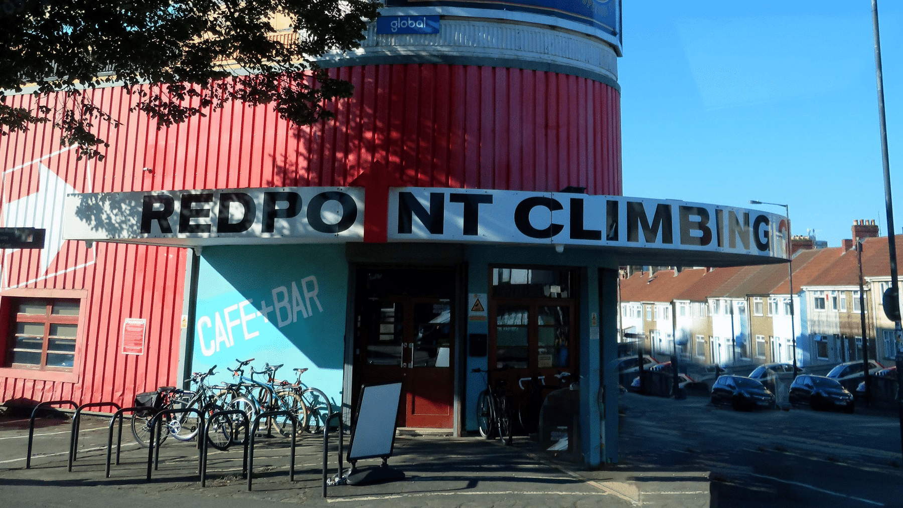 Entrance of a red building with a sign reading "Redpoint Climbing" and several bicycles parked outside.