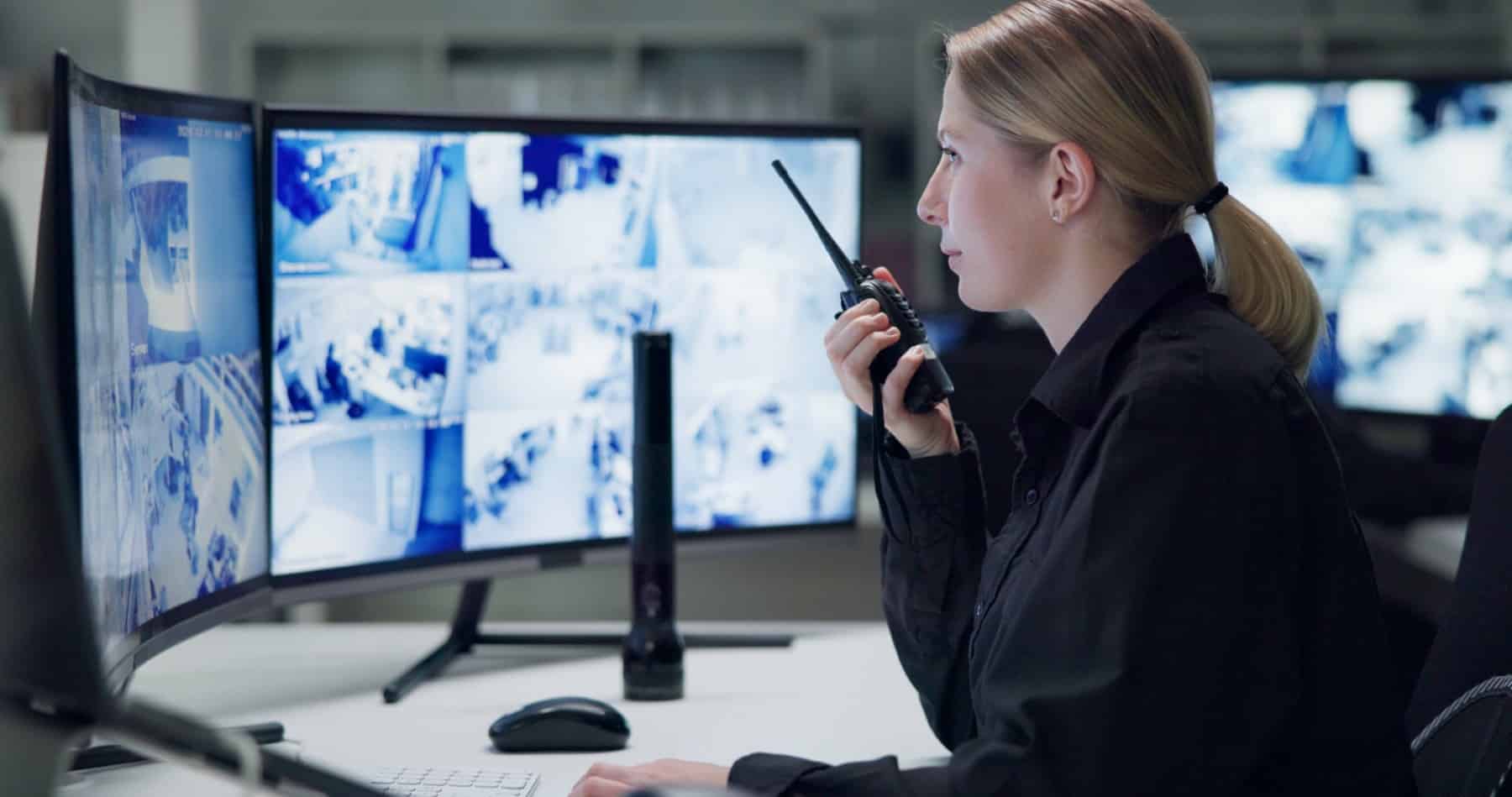 Watch, security and woman with radio, cctv and monitor for danger, talking and control room for guard. Desk, night and working for protection, safety and communication to backup and connection A woman monitors security cameras on multiple screens and speaks into a walkie-talkie.