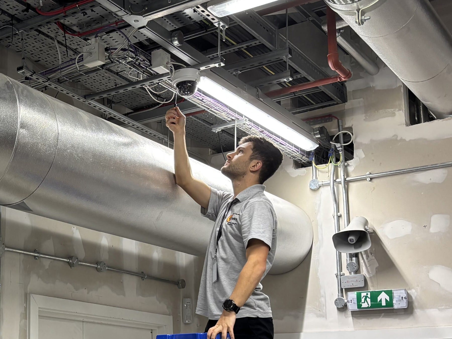A technician installs a security camera on the ceiling in an industrial building.