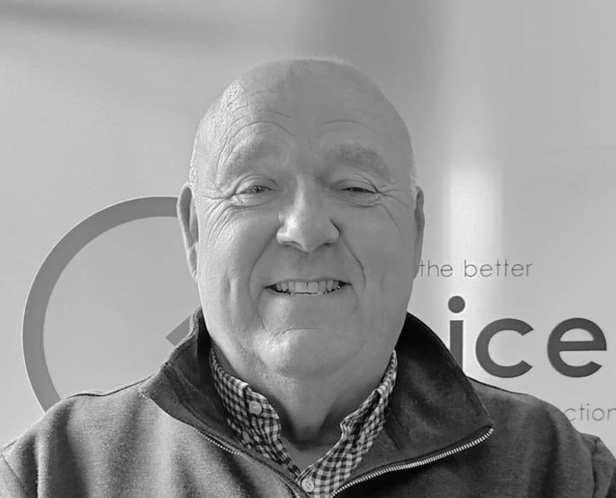 TonyEvans Smiling older man in a collared shirt and zip-up sweater, in front of a sign. Black and white photo.